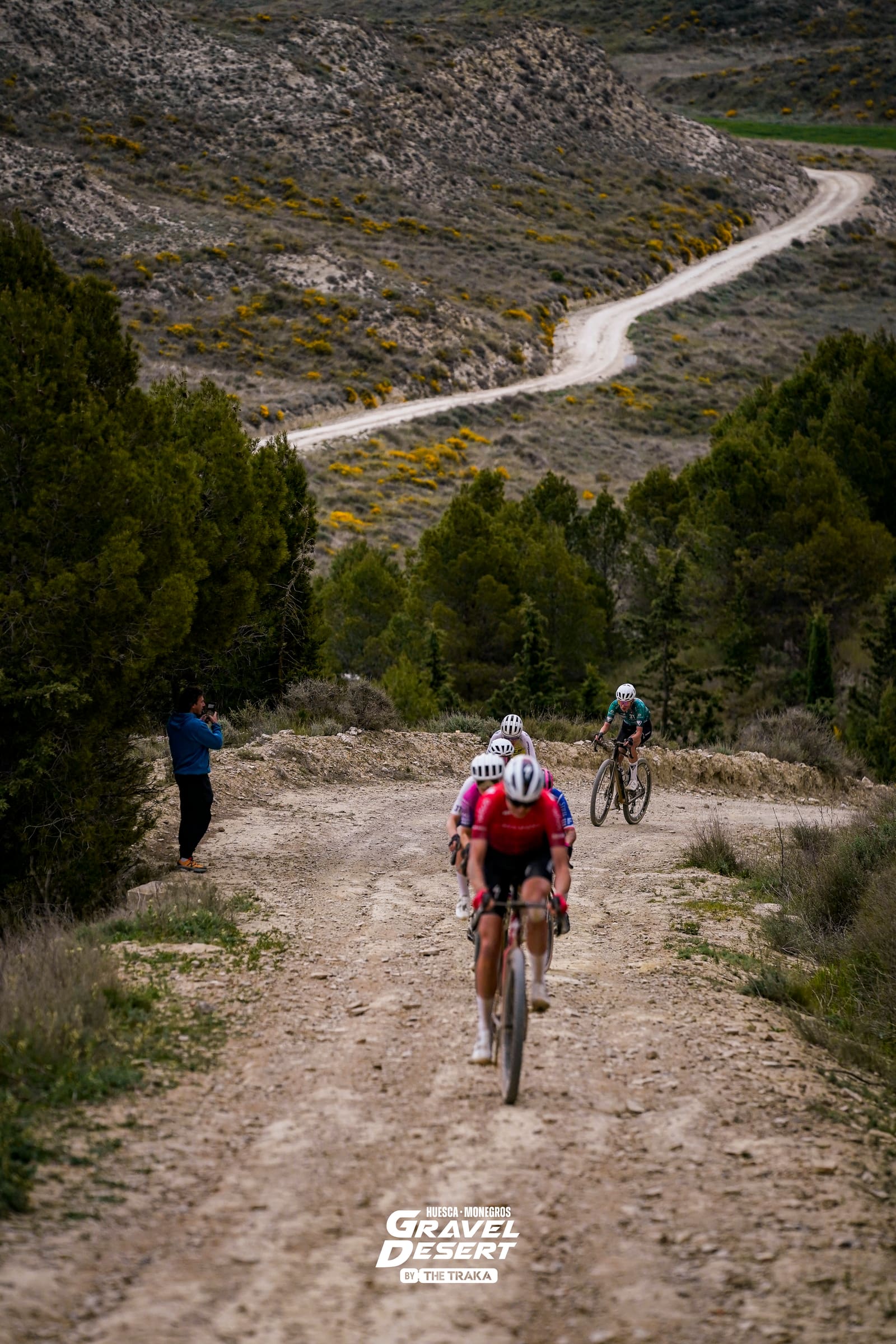 Ciclistas de gravel ascendiendo una pista de tierra en carrera, con el camino serpenteando hacia el horizonte